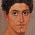 Pixelated portrait of a person with dark hair, light skin, and neutral expression against a muted background.