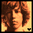 Pixelated profile portrait of a person with curly brown hair against warm-toned background, featuring small black heart symbol in bottom-right corner.