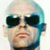 Pixelated static icon of a person wearing dark sunglasses with blue-tinted hair and visible facial features including nose, lips, and chin against a white background.