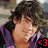 Pixelated close-up of a person with dark curly hair wearing purple clothing, holding a pink object near the face.