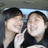 Two pixelated figures in close proximity, one with dark hair and light skin wearing a white top, the other with short dark hair and light skin in a black top against a blurred background.