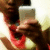 A person in a red shirt holds a silver smartphone, taking a selfie with their face partially visible and the phone screen reflecting light.