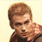 Pixelated static image of a person with light brown hair and dark clothing against a pale yellow background, rendered in low-resolution 8-bit style typical of early internet icons.