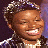 A split-screen image shows two versions of a person with short hair, one holding a microphone against a purple background and the other in front of a dark backdrop, both smiling widely.