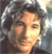 Pixelated close-up of a person's face with dark hair, wearing a dark jacket, against a blurred background with light and dark tones.