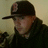 A person wearing a dark cap with a red emblem and dark clothing, shown in four with slight head and eye position changes