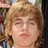Static pixelated image of a person with light brown curly hair, closed eyes, and a neutral expression against a blurred background.