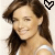 A woman with long brown hair in a white top, smiling slightly while looking left; the right side shows her face without a heart symbol above.