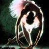 A stylized figure with a large white feathered headdress, dark brown hair, and a green and white outfit, posed in a dynamic stance against a dark background.