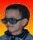 Two side-by-side pixelated portraits with orange-red gradient backgrounds; left figure wears dark sunglasses and blue clothing, right figure has short hair without glasses.