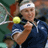 Static 48x48 pixel icon showing a tennis player in mid-swing with a yellow ball, wearing dark blue shirt and white headband against blurred green background.