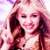 Pixelated static image of a person with long dark hair and light skin, wearing a white top against a blurred background with pink and purple tones.