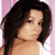 Pixelated close-up of a person with long dark hair against a pink background, showing shoulder and neck area.