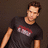 Pixelated image of a person in dark clothing with red and white text on shirt, next to brown background with pixelated text.