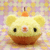 Pixelated yellow cupcake icon with brown base, orange top, black eyes, and red nose on pastel background.