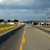 A pixelated road scene with a yellow center line, green fields, and buildings under a blue sky.