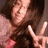 Pixelated image of a person with dark hair making a peace sign with their right hand, wearing a dark top with a pinkish-red shoulder area.