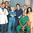 Group of people in medical scrubs and formal attire posing together, with a red banner reading 'HOSPITAL' visible behind them.