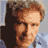 Pixelated static image of a person with light brown hair and fair skin, wearing dark clothing against a blurred background.