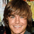 Pixelated close-up of a smiling person with brown hair against a blurred background of light and dark tones.