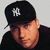 A person wearing a black cap with white NY logo, black shirt, and dark jacket, shown in four positions with subtle facial expression changes