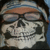 Static pixelated image of a skull wearing dark sunglasses and a brown headband, set against a blurred background with blue and gray tones.