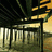 Static pixelated image of a dark structure with vertical bars and a horizontal beam, set against a gradient background of dark green and yellow tones.