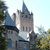 Pixelated image of a gray stone castle with blue-topped spires, surrounded by green foliage under a light blue sky.