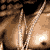 A 2x2 contact sheet of four animated frames showing a shirtless man with braided hair wearing multiple silver chains and a white headband against a dark brick wall background.