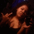 A woman with long dark hair in a black top poses against a dark background, making hand gestures.