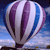 A pixelated hot air balloon with purple, white, and blue vertical stripes against a blue sky background.