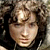 Pixelated static image of a person's face with curly hair, visible facial features including eyes and nose, and dark background elements.