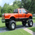 Animated image of an orange lifted Ford truck on grass with trees, next to text reading 'REAL MEN DRIVE BIG FORD TRUCKS' and a blue oval Ford logo.
