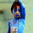 A child in a blue hooded outfit with patterned chest stands against a light green background, expression neutral.