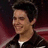 Pixelated close-up of a person with dark hair wearing a black jacket over a white shirt against a blurred red and dark background.