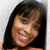 Pixelated close-up of a person with long dark hair, light skin, and a smiling expression against a light gray background.