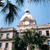 Pixelated image of a domed building with columns, green foliage, and a blue sky background, rendered in low-resolution style.