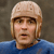 Pixelated image of a person wearing a light-colored helmet and blue shirt against a muted brown background.