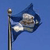 A pixelated blue flag on a pole against a solid blue background, with a white and brown emblem on the flag's surface.