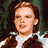 A pixelated image of a person with brown hair wearing a white shirt and brown vest on the left, next to bright pink background with green text reading "there's no place like home" on the right.