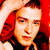 Pixelated static image of a person with red hair and light skin tone, wearing dark clothing against a bright red background.