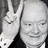 Pixelated grayscale image of a person with short hair making a peace sign, wearing dark clothing against a light background.