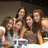 Group of five people with long brown hair posing closely together in a dimly lit setting, wearing casual clothing.