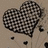 A pixelated heart shape with a checkered pattern on a light brown background, accompanied by scattered black dots.