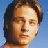 Pixelated static image of a person's face with brown hair against a blue background, rendered in low-resolution 256x256 pixels.