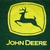 Yellow square with rounded corners containing a black deer silhouette, below which is yellow text reading JOHN DEERE on dark green background.