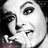 Black-and-white pixelated image of a person's face with dark hair, visible eye makeup, and partial facial features including nose and mouth.