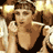 Pixelated static image of a person in motion with brown hair, wearing a black sleeveless top and holding an object near their face against a blurred background.