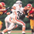 Static pixelated image of a football player in white uniform with red accents, surrounded by other players in darker uniforms on a field background.