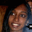 A static pixelated image shows a person with brown skin, dark hair, and light-colored eyes smiling broadly while holding an object near their face.